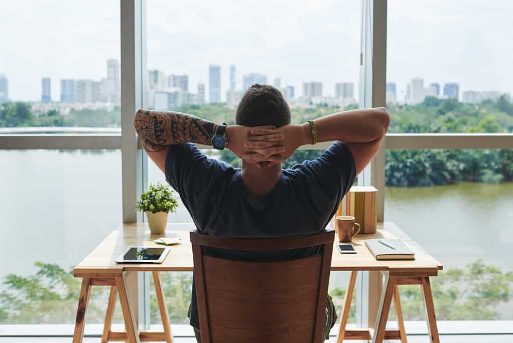 6-figure freelance web developer gazing out his desk window of his Singapore apartment pondering the question: Can web developers freelance? Tattooed and confident, he decides the answer is yes.
