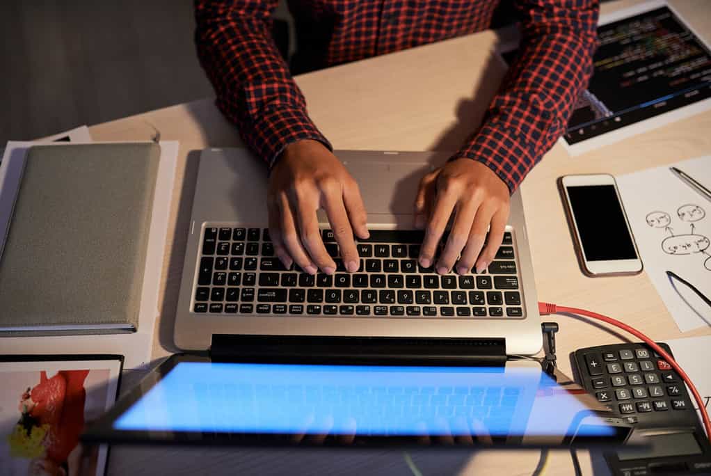 Hands of software engineer working on laptop at his office table at night