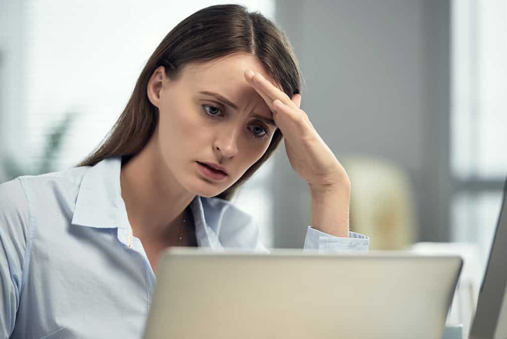 Young puzzled woman leaning on hand while using computer at workplace having problems with understanding